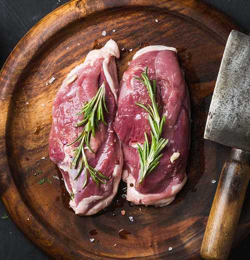 two pieces of raw duck meat displayed on a wooden cuttingboard