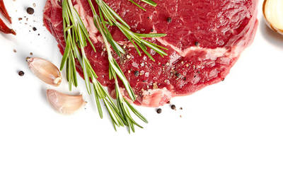 A steak with some chili peppers, seasons, garlic cloves, and a sliced onion