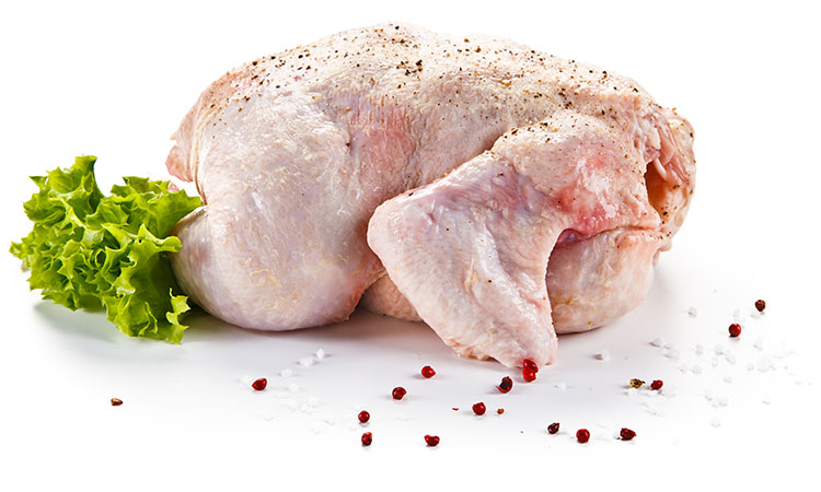 A whole raw chicken laying on its front, covered in spices